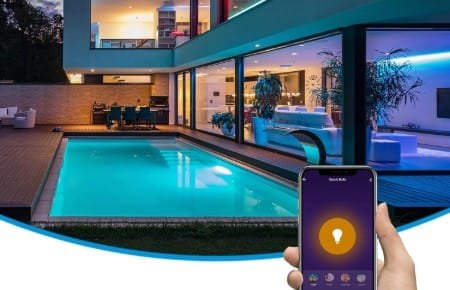 Bombillas decorativas controladas mediante un smartphone iluminando una piscina y los interiores de una vivienda de grandes ventanales con luces azules y cálidas